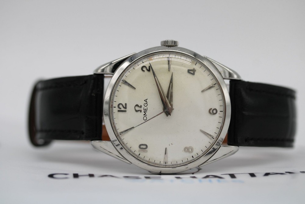 A 1960s Omega stainless steel manual-wind wristwatch featuring a silver dial with silver-toned Arabic numerals and indices on a black leather strap. View XII