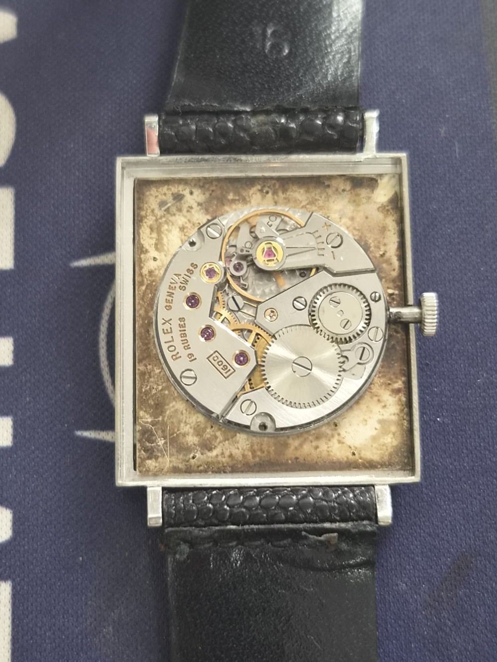 A 1960s square Rolex Cellini wristwatch featuring an 18ct white gold case, silver sunburst dial with simple index markers, and a black textured leather strap. View V