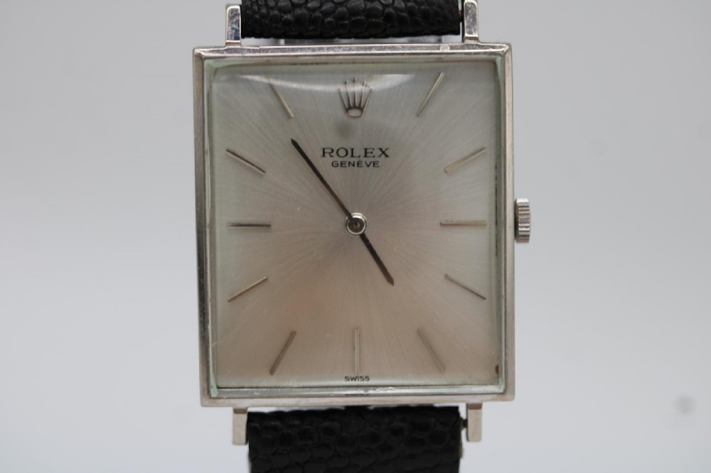 A 1960s square Rolex Cellini wristwatch featuring an 18ct white gold case, silver sunburst dial with simple index markers, and a black textured leather strap. View VII