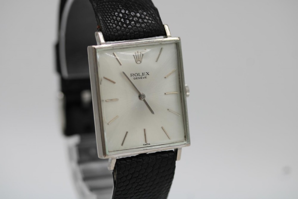 A 1960s square Rolex Cellini wristwatch featuring an 18ct white gold case, silver sunburst dial with simple index markers, and a black textured leather strap. View VIII