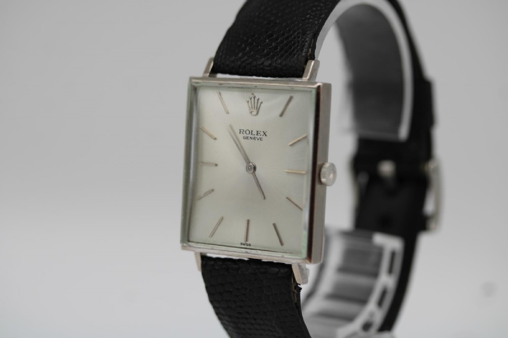 A 1960s square Rolex Cellini wristwatch featuring an 18ct white gold case, silver sunburst dial with simple index markers, and a black textured leather strap. View IX
