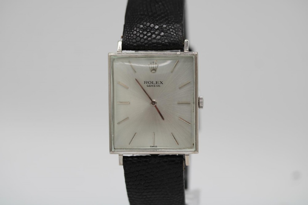 A 1960s square Rolex Cellini wristwatch featuring an 18ct white gold case, silver sunburst dial with simple index markers, and a black textured leather strap. View X