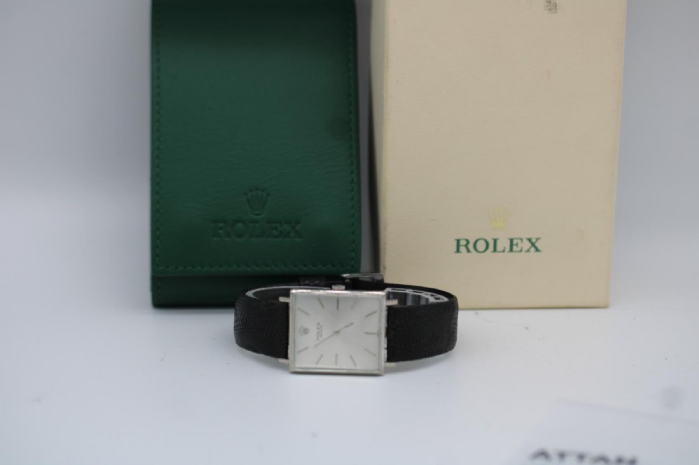 A 1960s square Rolex Cellini wristwatch featuring an 18ct white gold case, silver sunburst dial with simple index markers, and a black textured leather strap. View XIV