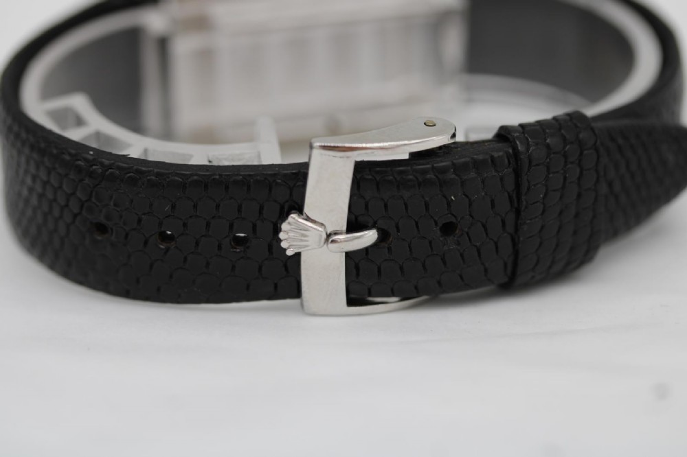 A 1960s square Rolex Cellini wristwatch featuring an 18ct white gold case, silver sunburst dial with simple index markers, and a black textured leather strap. View XV