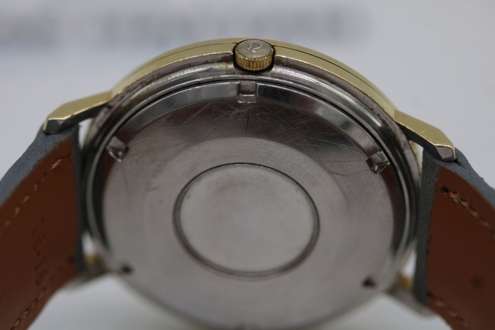 A circular 14ct gold vintage Omega Constellation wristwatch featuring a cream dial with gold baton markers, dauphine hands, date window, and a grey leather strap. View III