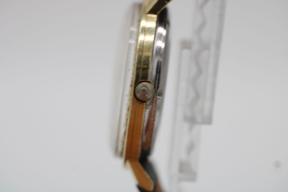 A circular 14ct gold vintage Omega Constellation wristwatch featuring a cream dial with gold baton markers, dauphine hands, date window, and a grey leather strap. View VI