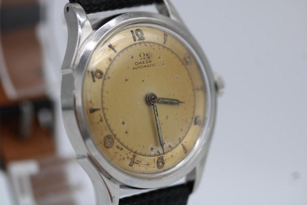 A round 1947 stainless steel Omega wristwatch displaying an aged cream dial with Arabic numerals and fitted with a black textured leather strap. View III