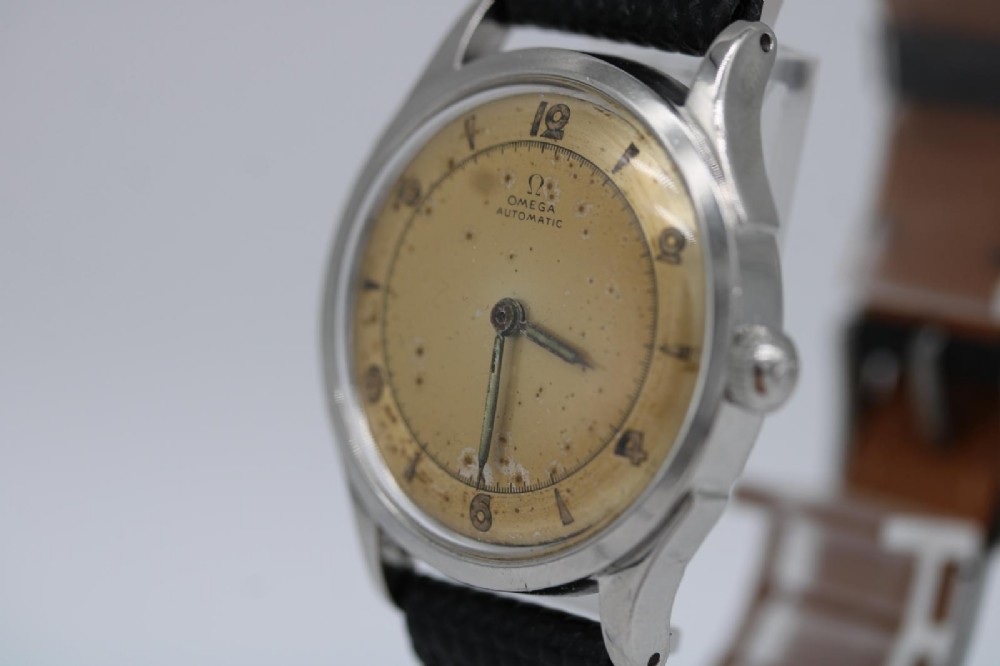 A round 1947 stainless steel Omega wristwatch displaying an aged cream dial with Arabic numerals and fitted with a black textured leather strap. View IV