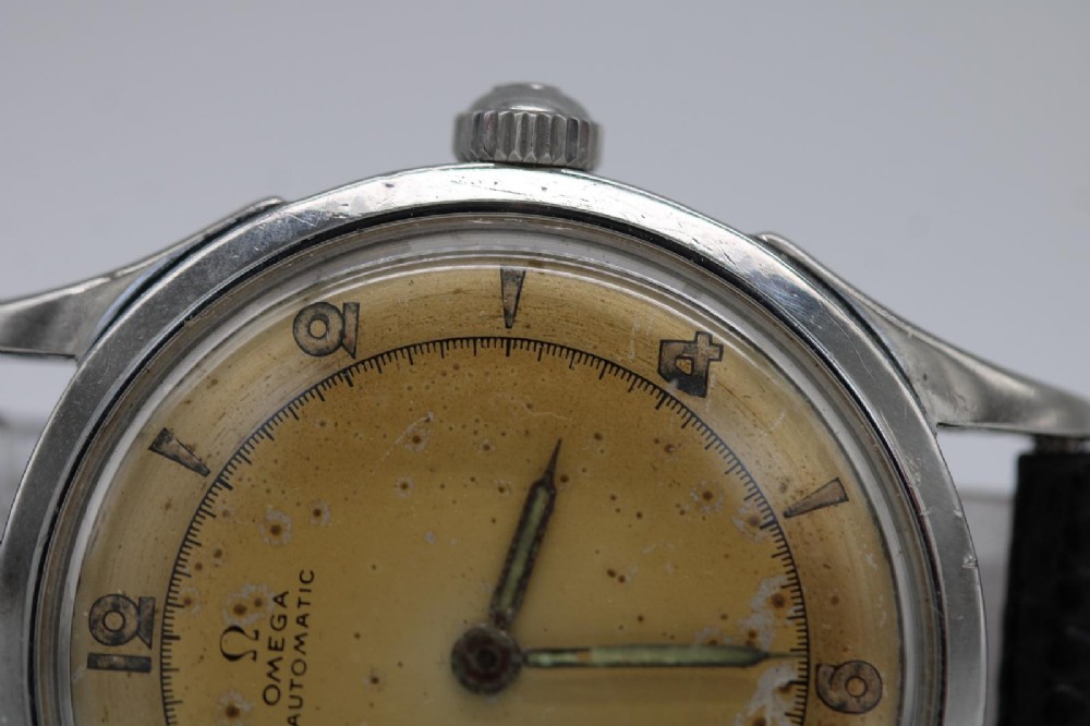 A round 1947 stainless steel Omega wristwatch displaying an aged cream dial with Arabic numerals and fitted with a black textured leather strap. View V