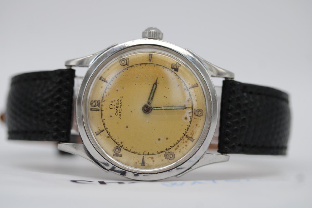 A round 1947 stainless steel Omega wristwatch displaying an aged cream dial with Arabic numerals and fitted with a black textured leather strap. View VI