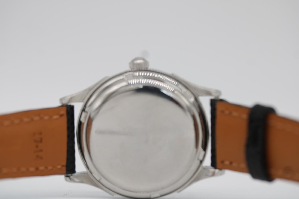 A round 1947 stainless steel Omega wristwatch displaying an aged cream dial with Arabic numerals and fitted with a black textured leather strap. View VII