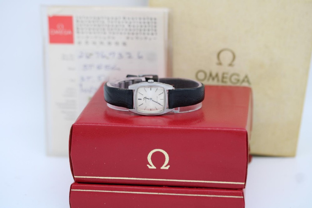 A vintage 1968 ladies Omega De Ville stainless steel wristwatch featuring a tonneau-shaped case, silvered dial, and black leather strap.