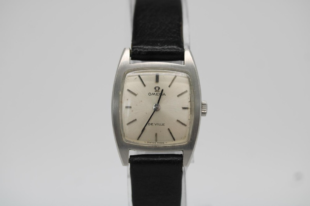 A vintage 1968 ladies Omega De Ville stainless steel wristwatch featuring a tonneau-shaped case, silvered dial, and black leather strap. View VI