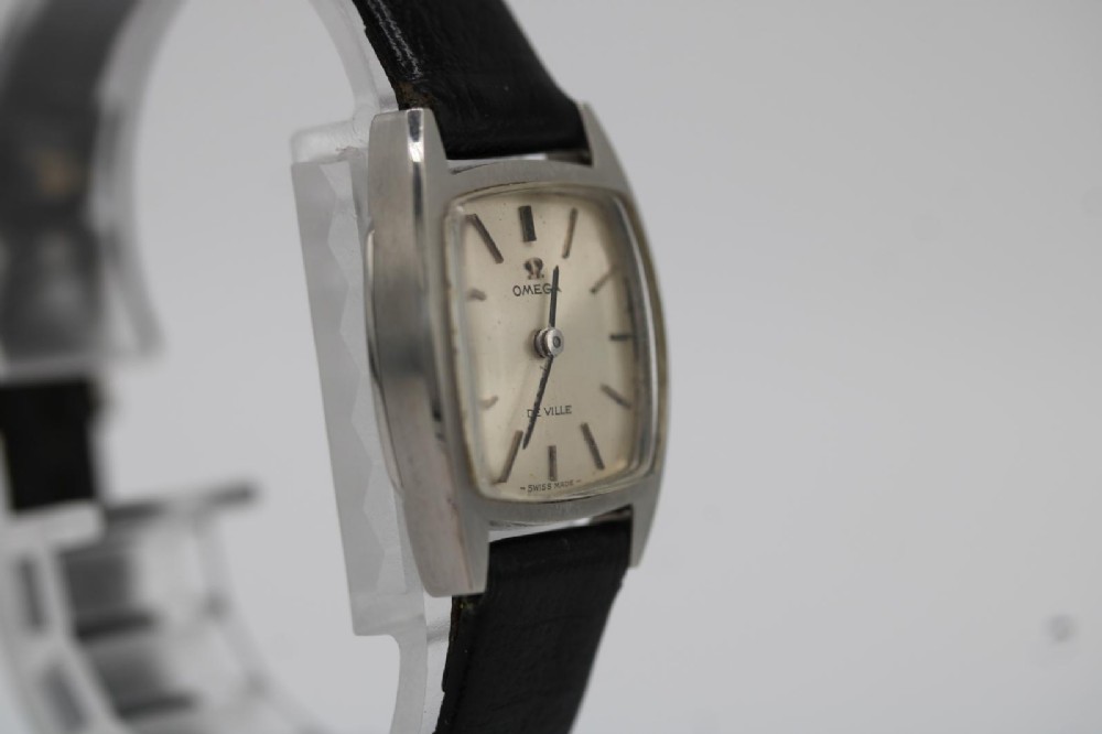 A vintage 1968 ladies Omega De Ville stainless steel wristwatch featuring a tonneau-shaped case, silvered dial, and black leather strap. View VII