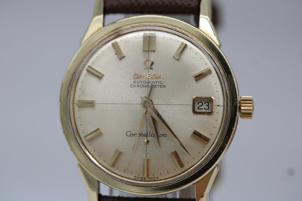 A 1962 vintage Omega Constellation wristwatch featuring a gold pie-pan dial, date aperture, and brown leather strap. View VII