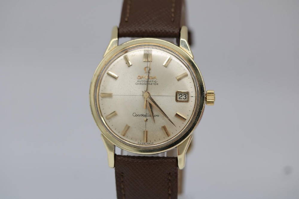 A 1962 vintage Omega Constellation wristwatch featuring a gold pie-pan dial, date aperture, and brown leather strap.