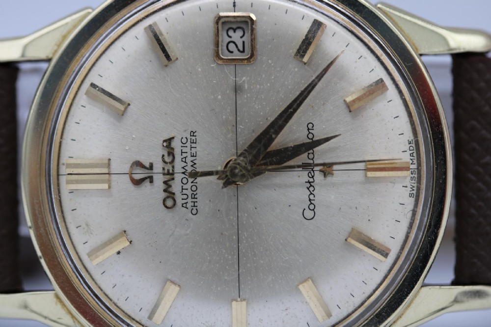 A 1962 vintage Omega Constellation wristwatch featuring a gold pie-pan dial, date aperture, and brown leather strap. View X