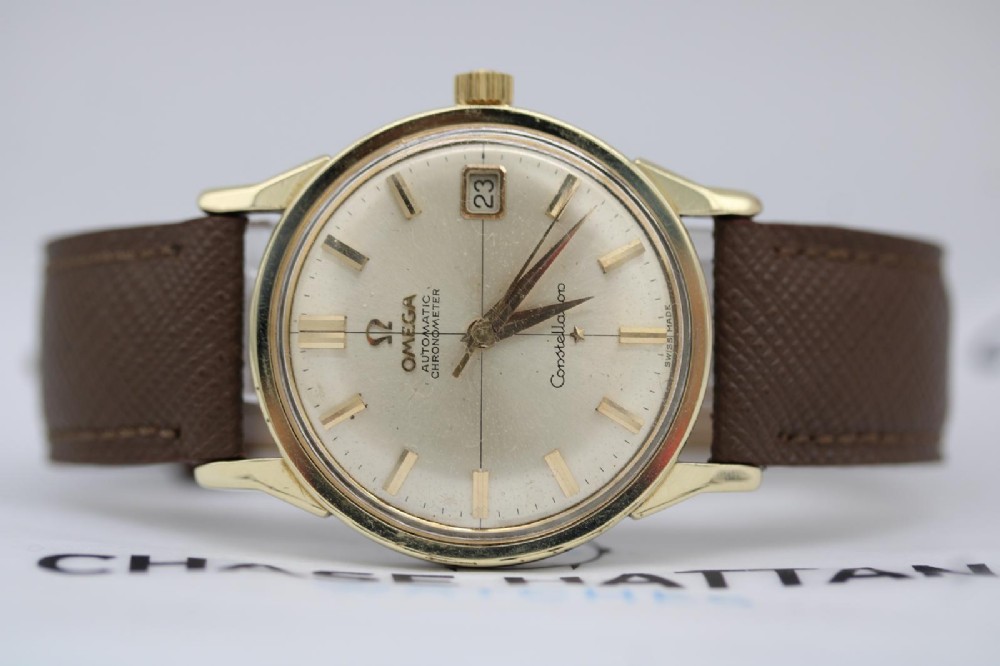A 1962 vintage Omega Constellation wristwatch featuring a gold pie-pan dial, date aperture, and brown leather strap. View XI
