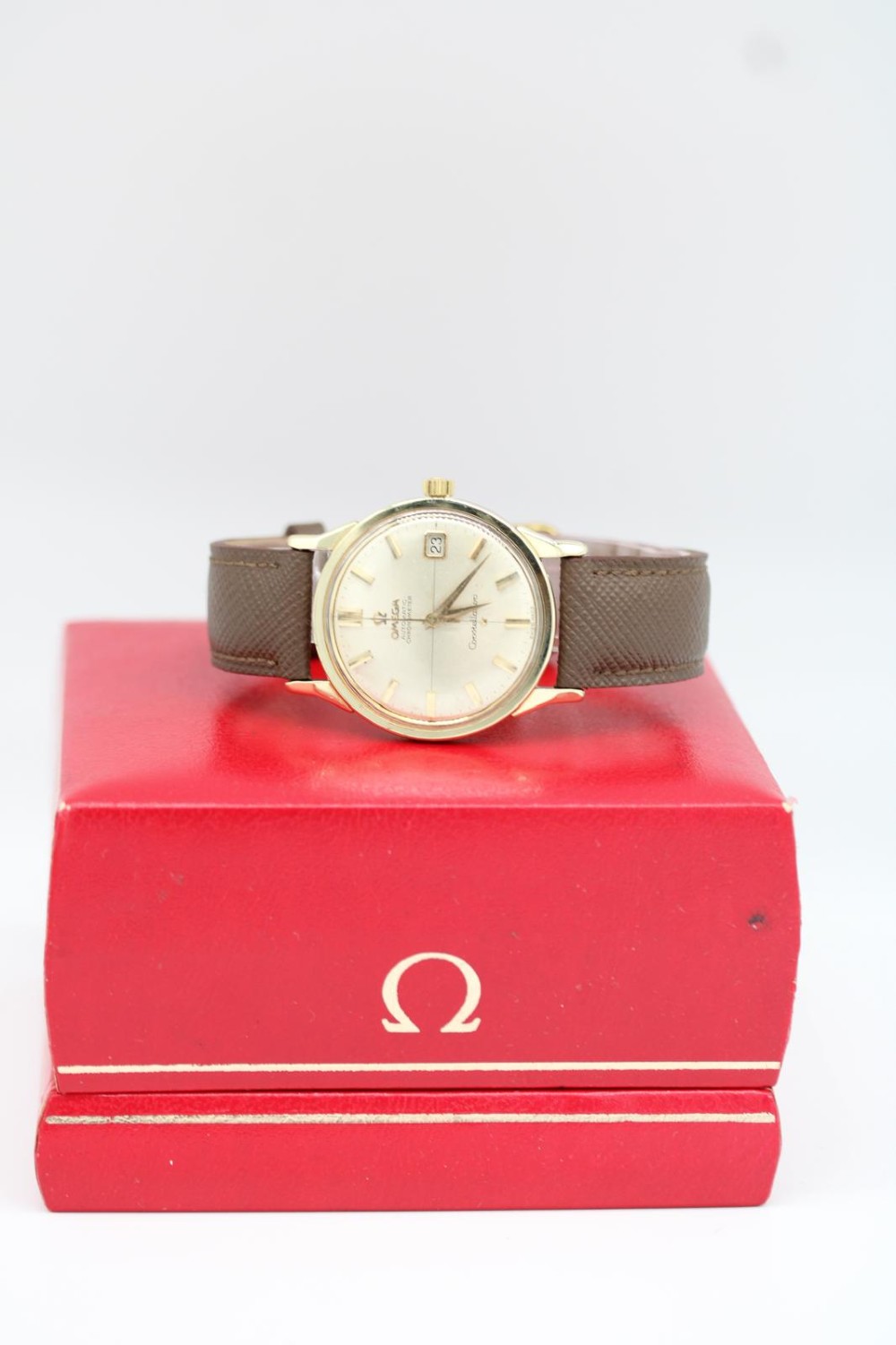 A 1962 vintage Omega Constellation wristwatch featuring a gold pie-pan dial, date aperture, and brown leather strap. View XII