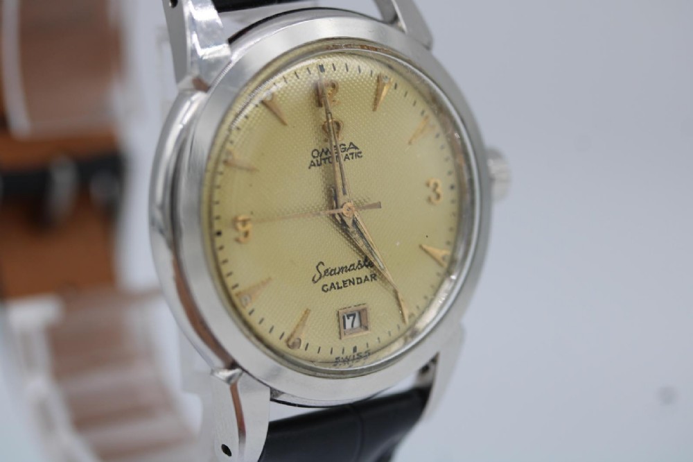 A vintage 1952 Omega Seamaster Calendar wristwatch featuring a stainless steel case, textured gold-coloured dial with date display at six oclock, and a black leather strap. View IV