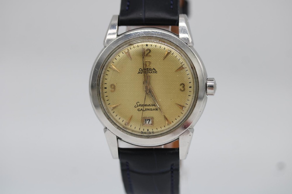 A vintage 1952 Omega Seamaster Calendar wristwatch featuring a stainless steel case, textured gold-coloured dial with date display at six oclock, and a black leather strap.