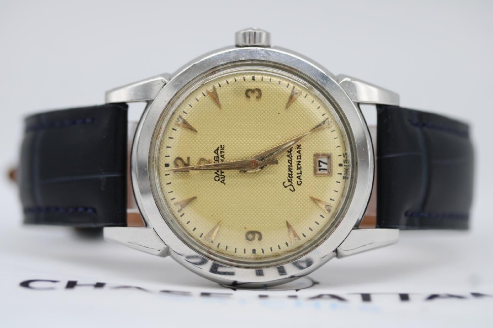 A vintage 1952 Omega Seamaster Calendar wristwatch featuring a stainless steel case, textured gold-coloured dial with date display at six oclock, and a black leather strap. View IX
