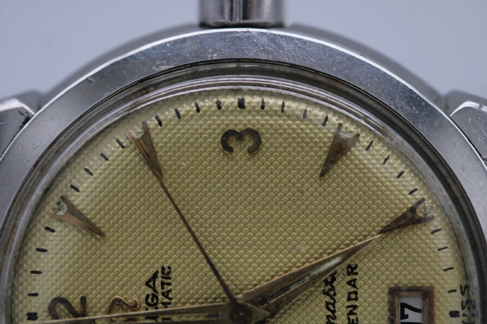 A vintage 1952 Omega Seamaster Calendar wristwatch featuring a stainless steel case, textured gold-coloured dial with date display at six oclock, and a black leather strap. View XI