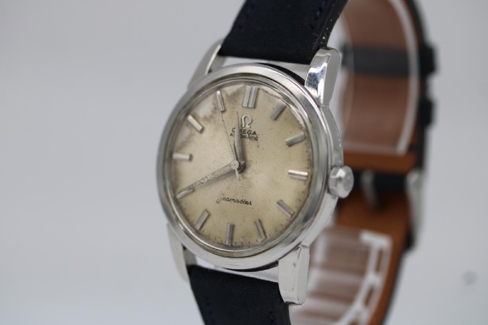 A 1950s stainless steel Omega Seamaster wristwatch featuring a patinated cream dial with silver baton indices and a black leather strap. View IV