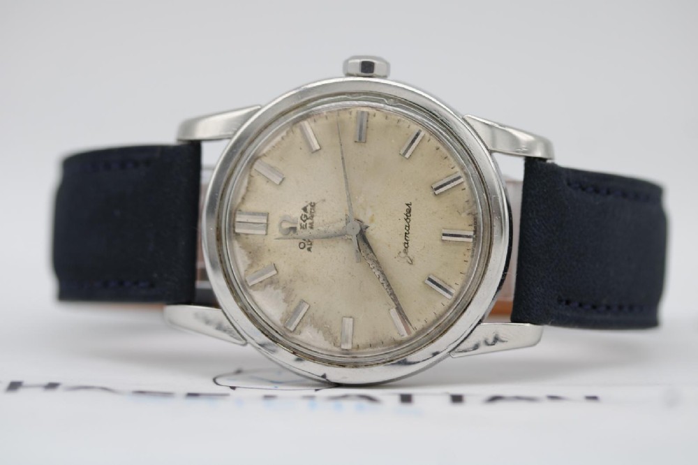 A 1950s stainless steel Omega Seamaster wristwatch featuring a patinated cream dial with silver baton indices and a black leather strap. View VI