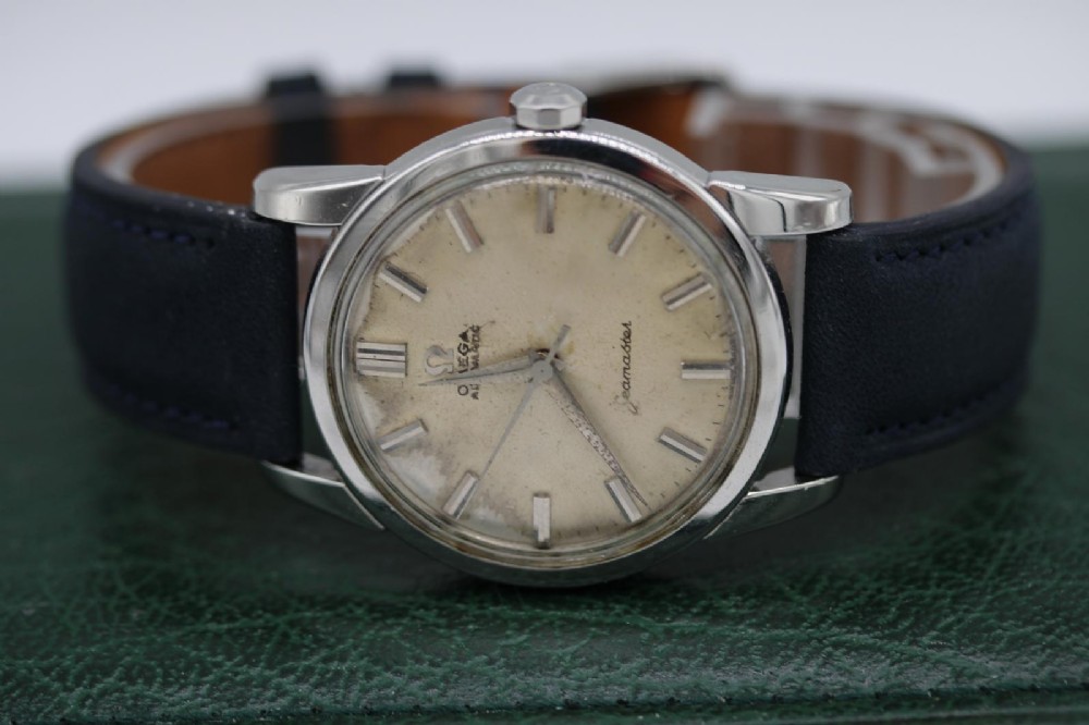A 1950s stainless steel Omega Seamaster wristwatch featuring a patinated cream dial with silver baton indices and a black leather strap. View VII