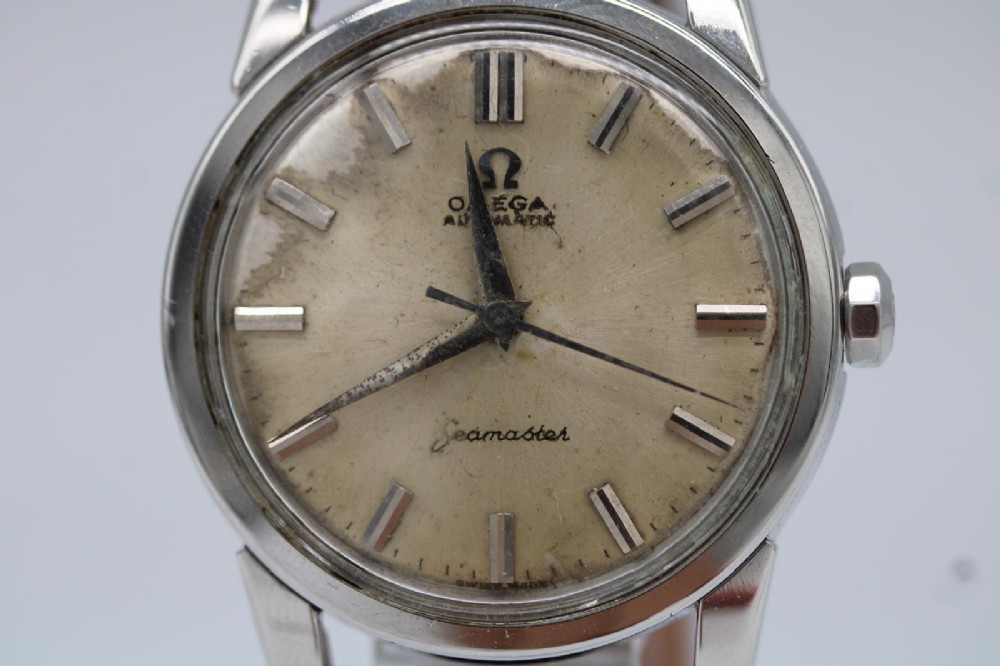 A 1950s stainless steel Omega Seamaster wristwatch featuring a patinated cream dial with silver baton indices and a black leather strap. View IX
