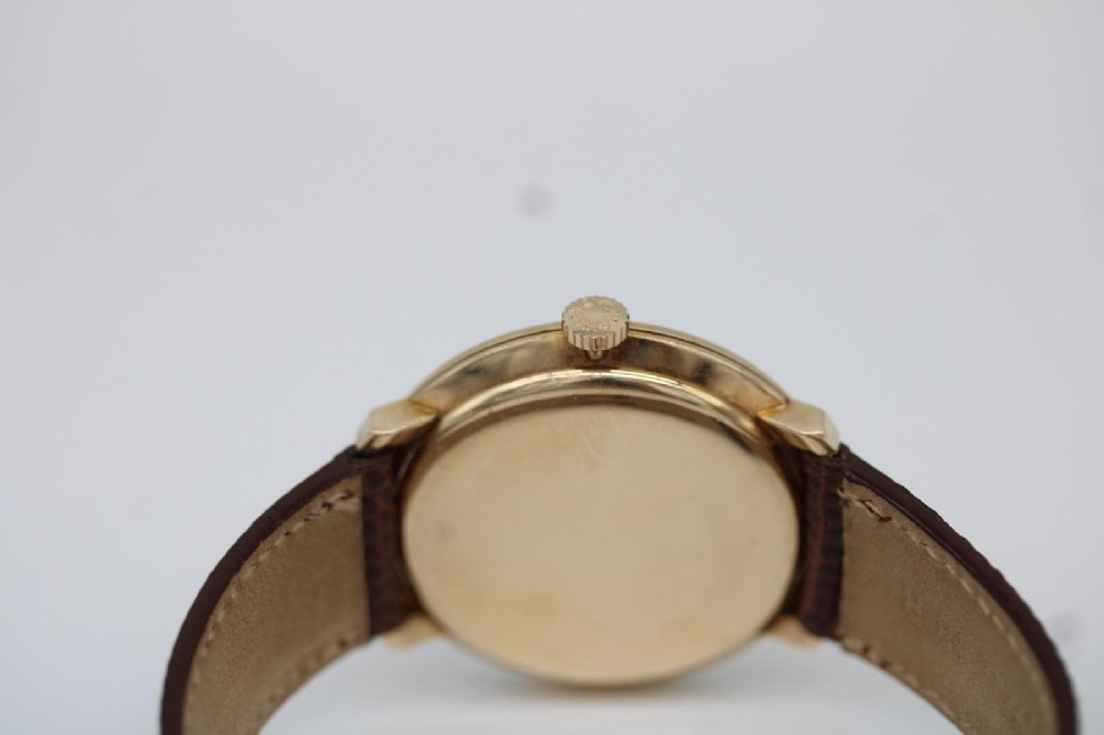 A vintage circular 9ct gold wristwatch by Longines featuring a silver dial with gold baton hour markers and a brown leather strap. View IX