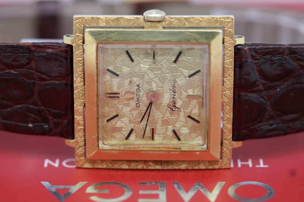 A 1960s Omega Geneve manual wind wristwatch featuring an 18ct yellow gold cushion-shaped case, a dark brown dial with gold Roman numerals at twelve and six, and a brown leather strap. View II