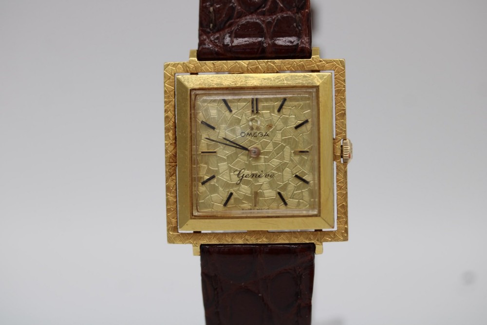 A 1960s Omega Geneve manual wind wristwatch featuring an 18ct yellow gold cushion-shaped case, a dark brown dial with gold Roman numerals at twelve and six, and a brown leather strap. View IV