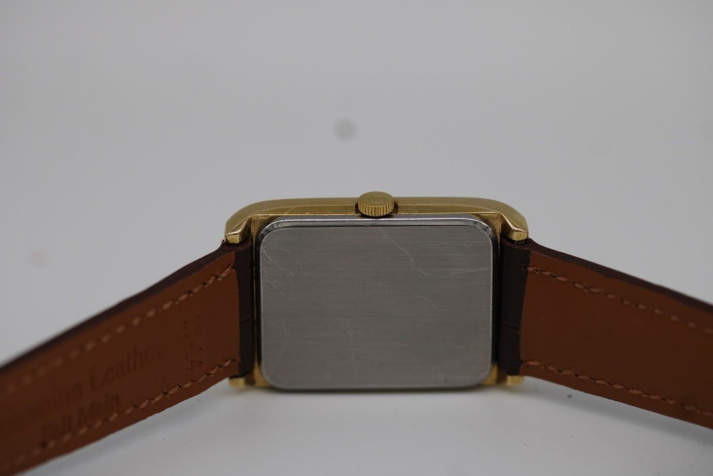 A 1960s Omega Geneve manual wind wristwatch featuring an 18ct yellow gold cushion-shaped case, a dark brown dial with gold Roman numerals at twelve and six, and a brown leather strap. View IX