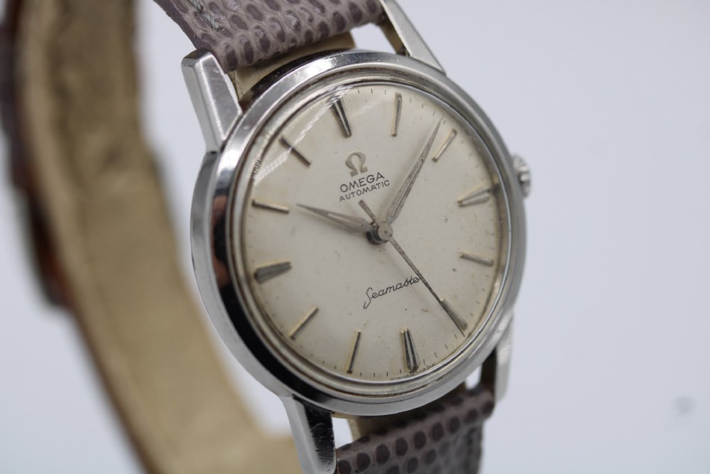 A vintage 1960 Omega Seamaster automatic wristwatch with a stainless steel case, silver cream dial, and grey textured leather strap. View IV