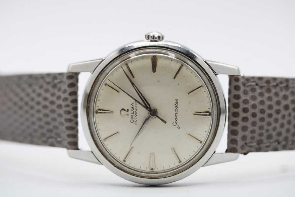 A vintage 1960 Omega Seamaster automatic wristwatch with a stainless steel case, silver cream dial, and grey textured leather strap. View VI