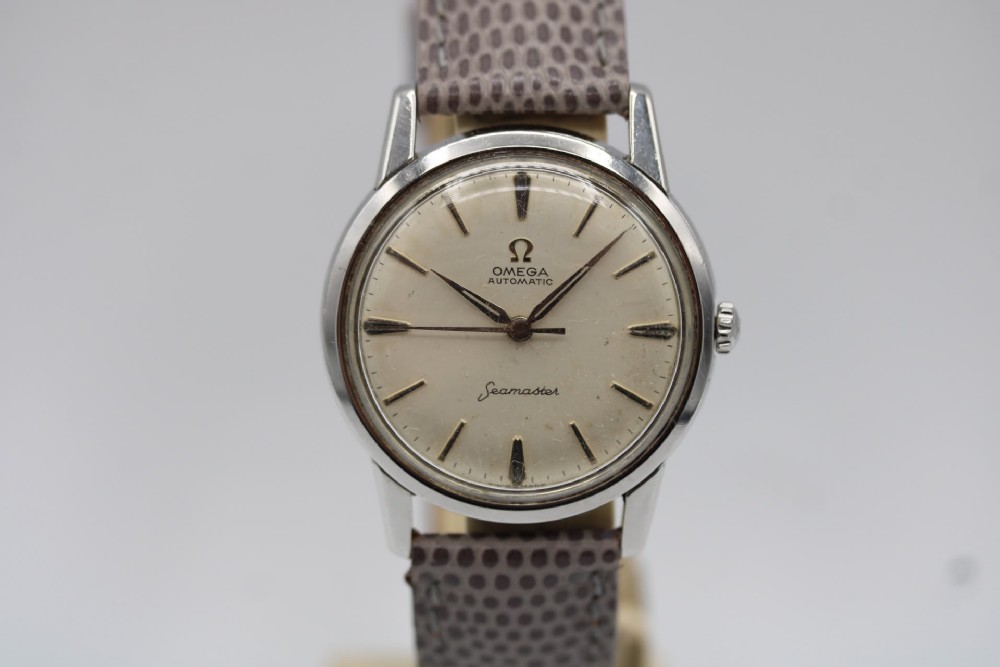 A vintage 1960 Omega Seamaster automatic wristwatch with a stainless steel case, silver cream dial, and grey textured leather strap.