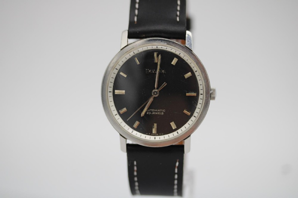 A vintage Bulova automatic wristwatch featuring a black dial with silver baton hour markers and a black leather strap with white stitching. View III