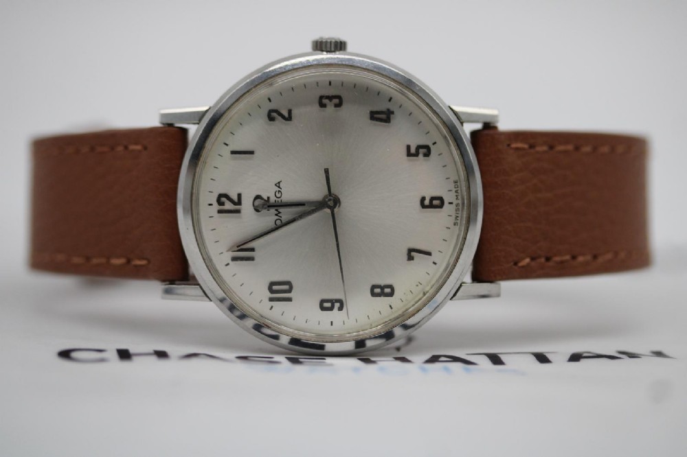 A 1967 stainless steel Omega wristwatch featuring a white dial with black Arabic numerals and a tan brown leather strap. View II