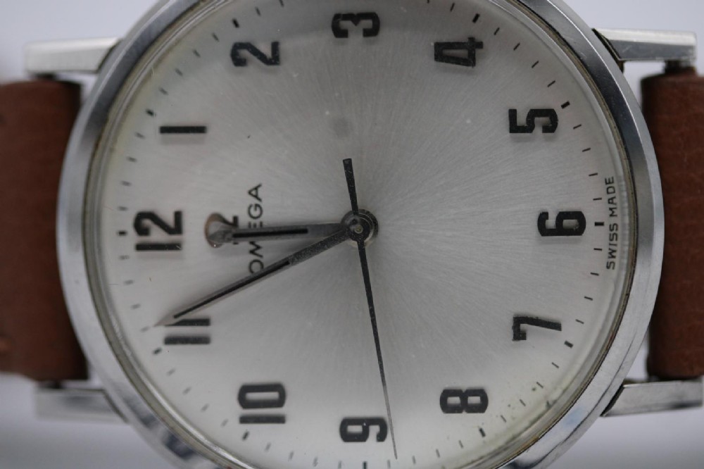 A 1967 stainless steel Omega wristwatch featuring a white dial with black Arabic numerals and a tan brown leather strap. View III