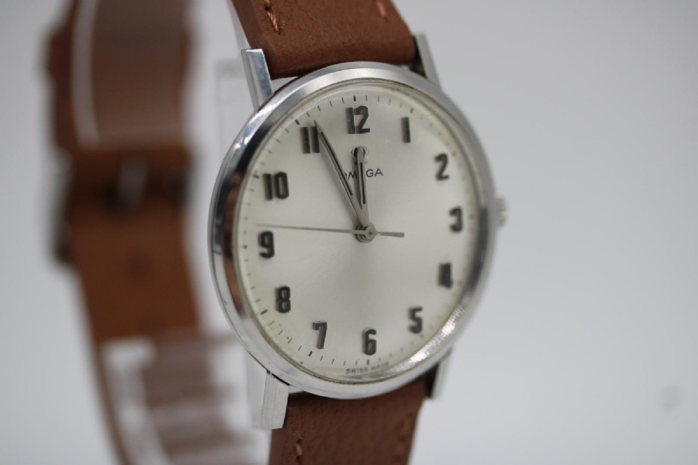 A 1967 stainless steel Omega wristwatch featuring a white dial with black Arabic numerals and a tan brown leather strap. View VI