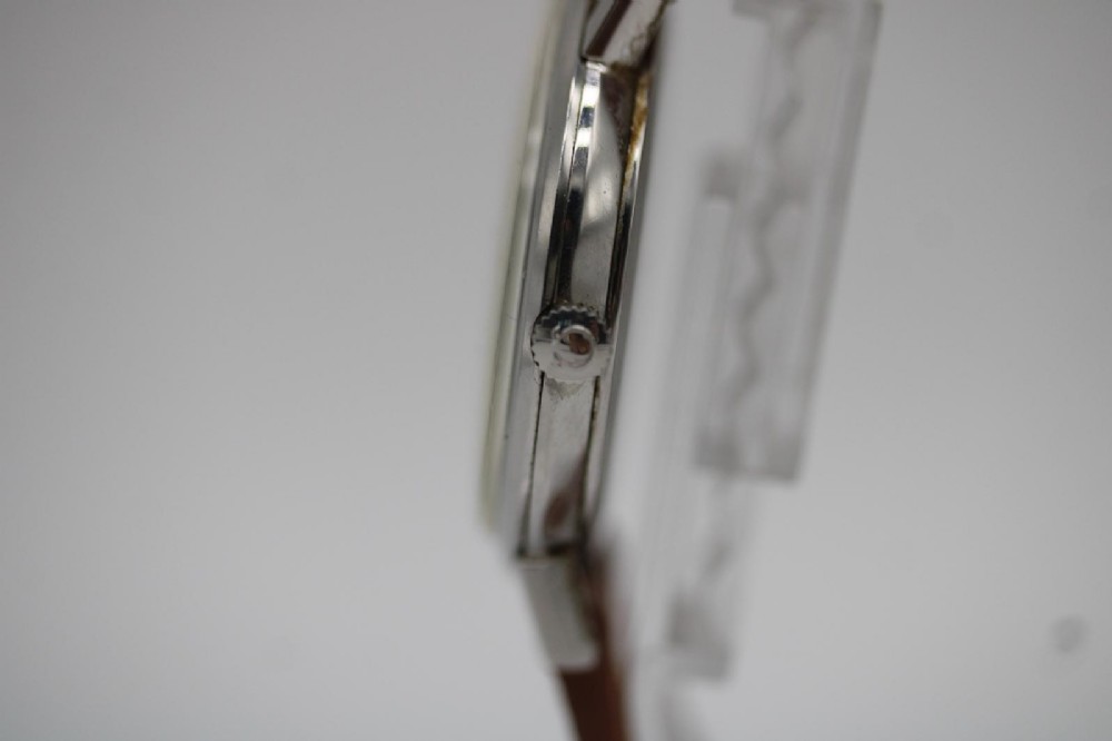 A 1967 stainless steel Omega wristwatch featuring a white dial with black Arabic numerals and a tan brown leather strap. View VII