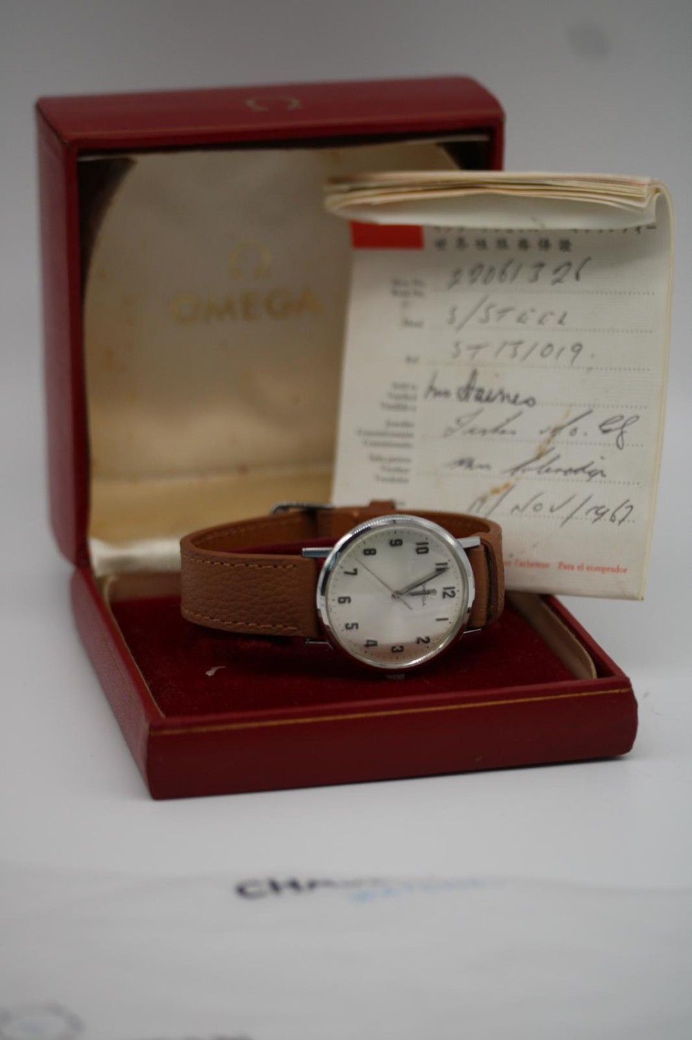 A 1967 stainless steel Omega wristwatch featuring a white dial with black Arabic numerals and a tan brown leather strap. View IX
