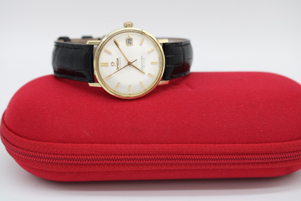 A vintage gold-plated Omega Seamaster DeVille automatic wristwatch with a white textured dial, gold baton indices, date window, and black leather strap. View II