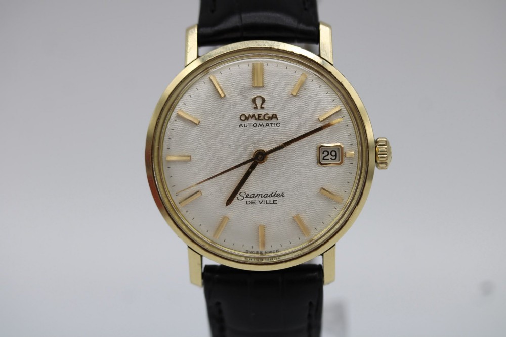 A vintage gold-plated Omega Seamaster DeVille automatic wristwatch with a white textured dial, gold baton indices, date window, and black leather strap. View VII