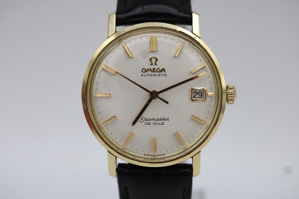 A vintage gold-plated Omega Seamaster DeVille automatic wristwatch with a white textured dial, gold baton indices, date window, and black leather strap. View VIII
