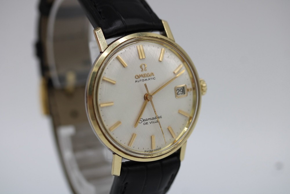 A vintage gold-plated Omega Seamaster DeVille automatic wristwatch with a white textured dial, gold baton indices, date window, and black leather strap. View XI