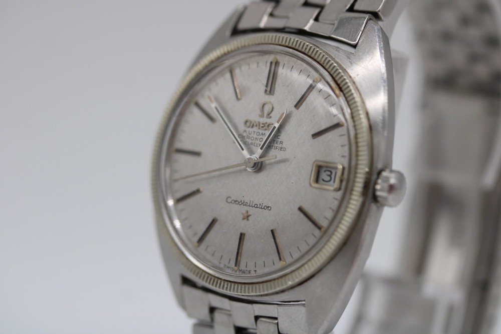 A 1969 vintage Omega Constellation wristwatch featuring a stainless steel case, fluted bezel, silver linen dial, date window, and steel link bracelet. View VI