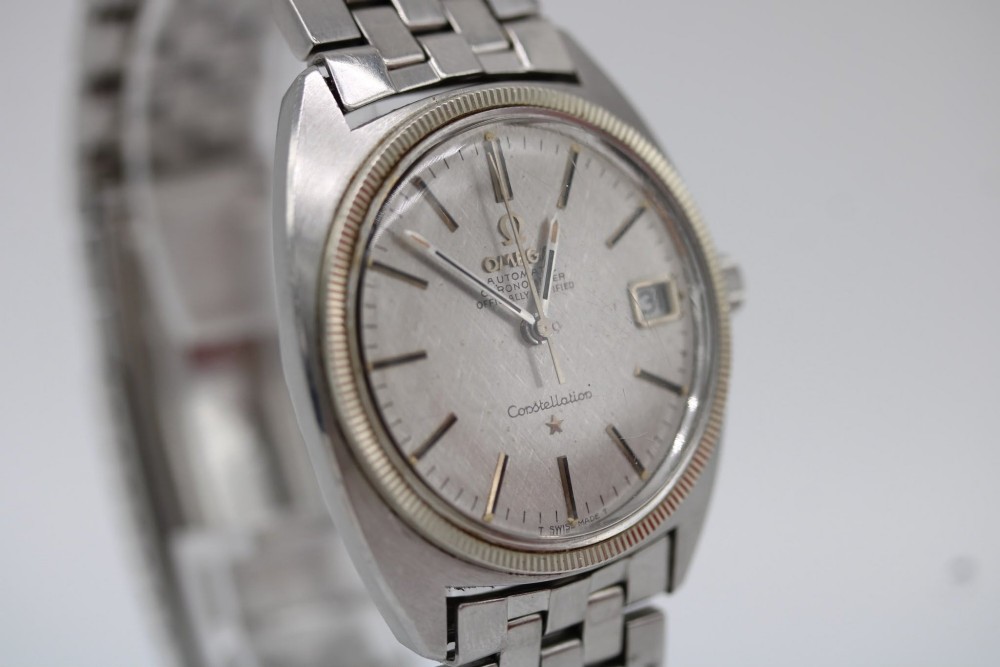 A 1969 vintage Omega Constellation wristwatch featuring a stainless steel case, fluted bezel, silver linen dial, date window, and steel link bracelet. View XI